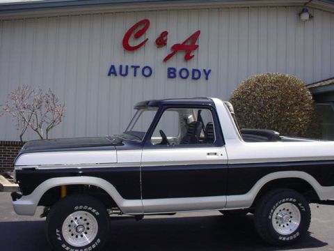 1979 Ford Bronco - A two-tone black and white Ford Bronco is parked outside an auto body shop.