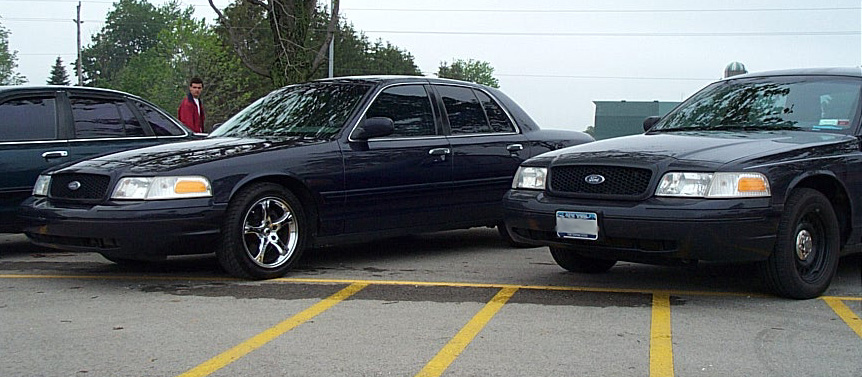 Three dark Ford Crown Victoria sedans parked in a row, center car on chrome aftermarket wheels