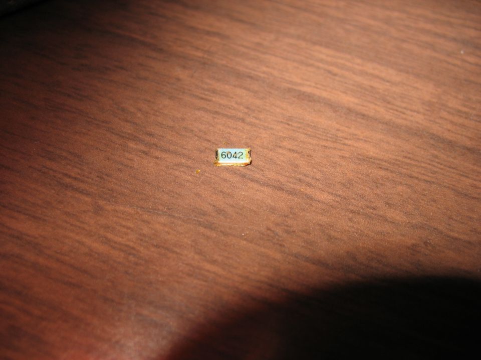 Small rectangular electronic component with '6042' printed on it, resting on a wooden surface