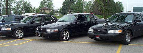2001 Ford Crown Victoria - Three black sedans are parked in a lot, two of which appear to be Ford Crown Victorias.
