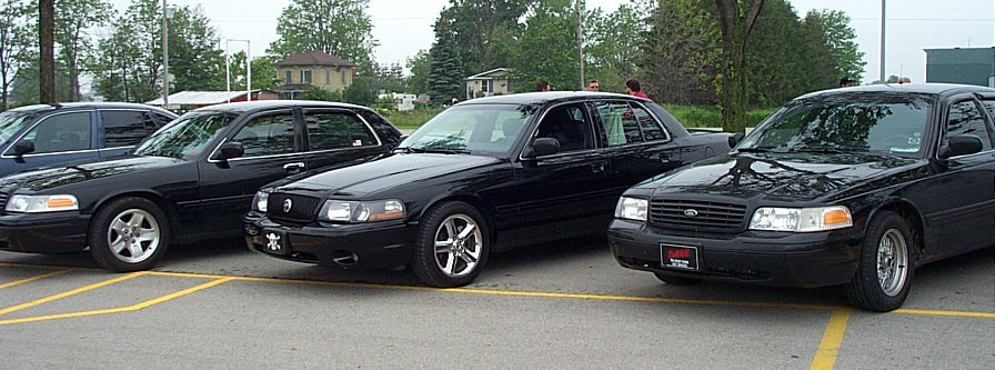 Three black sedans parked in a lot, two are Ford Crown Victorias