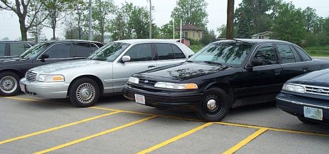 2001 Ford Crown Victoria - Multiple Ford Crown Victorias are parked in a lot, with yellow lines marking the parking spaces.