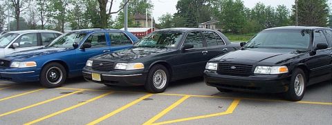 2001 Ford Crown Victoria - Three Ford Crown Victorias are parked in a lot, showing their front ends.