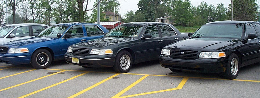 Three Ford Crown Victorias parked in a lot, two black and one blue
