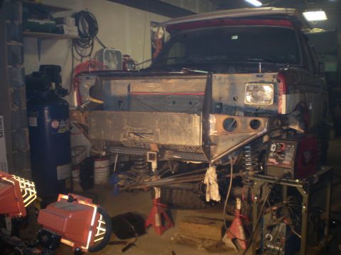 1986 Ford Bronco - The front end of a Ford Bronco is being worked on in a garage, with welding equipment nearby.