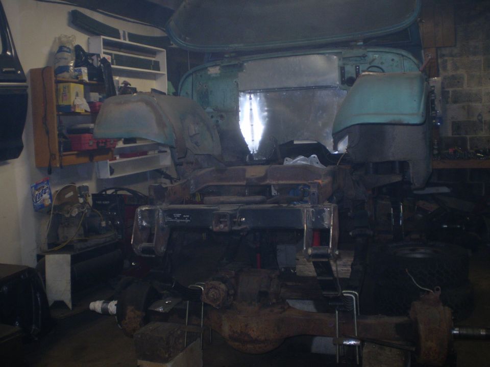 Chassis of a vehicle in a garage, looks like it's being worked on. Some shelves with parts are visible