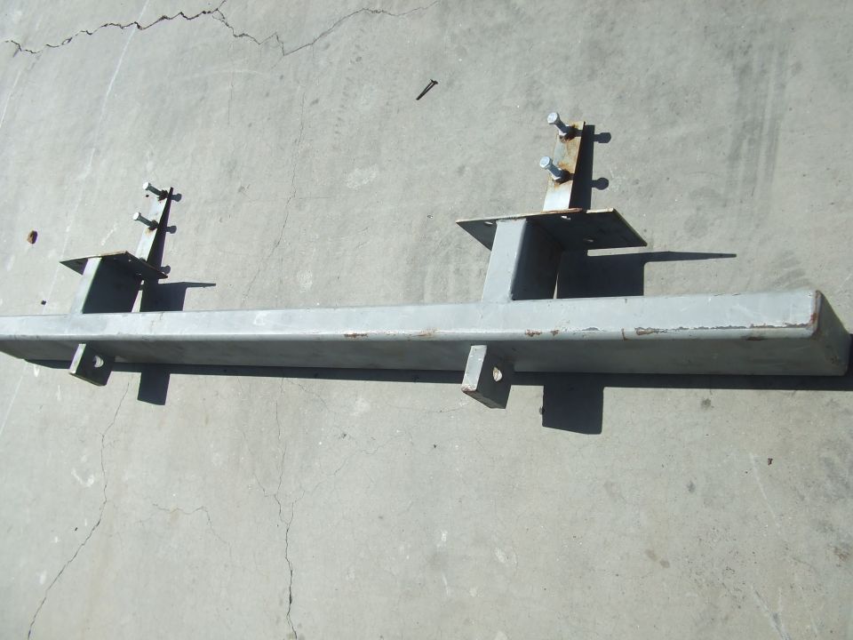 A fabricated gray steel frame crossmember bracket on concrete