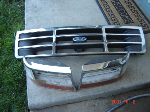 1993 Ford Bronco - Grille and headlight bezels from a 1993 Ford Bronco are laid out on a concrete surface.