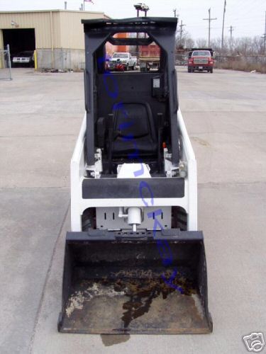 1946 Ford F1 - Front view of a skid steer loader with a loaded bucket, parked outdoors near a building.