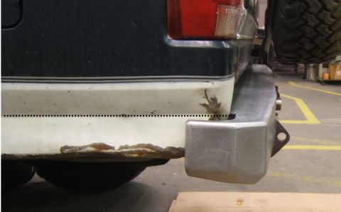 1995 Ford Bronco - The rear of a vehicle displays significant rust on its bumper and lower body panel.