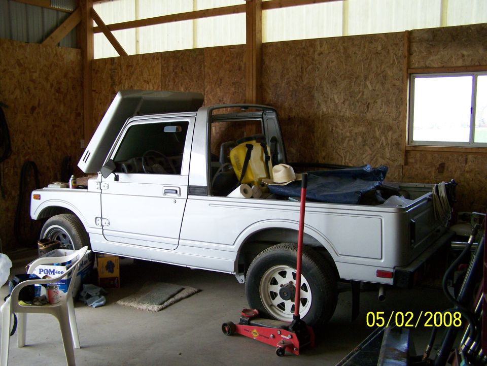 Side view of a small silver soft-top SUV pickup inside a barn