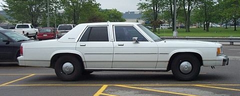 2001 Ford Crown Victoria - A white 2001 Ford Crown Victoria sedan is parked in a lot, seen from the side.