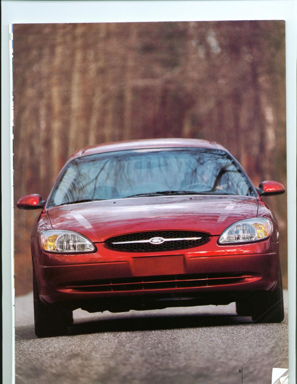 Front view of a red Ford Taurus sedan on a tree-lined road