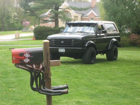 1995 Ford Bronco - A black SUV sits on a grassy lawn in front of a house, with a unique mailbox in the foreground.