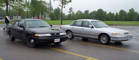 2001 Ford Crown Victoria - Two Ford Crown Victorias, a black and a silver model, are parked in an outdoor lot.