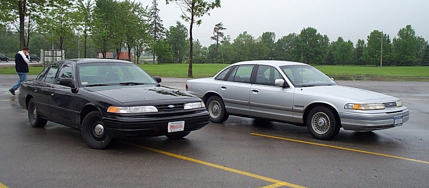 Two 2001 Ford Crown Victorias parked side-by-side on a wet asphalt lot