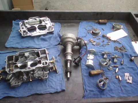 1984 Ford Bronco - Various engine parts, including carburetors and a distributor, are organized on a workbench.