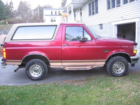 1995 Ford Bronco - Side view of a red Ford Bronco with a tan removable top, parked in a driveway.