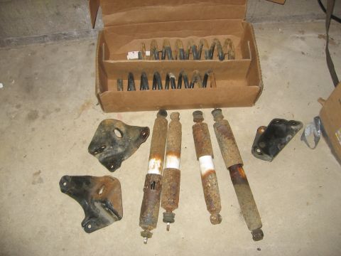 1995 Ford Bronco - A collection of used shock absorbers and coil springs are laid out on a concrete floor next to a cardboard box.
