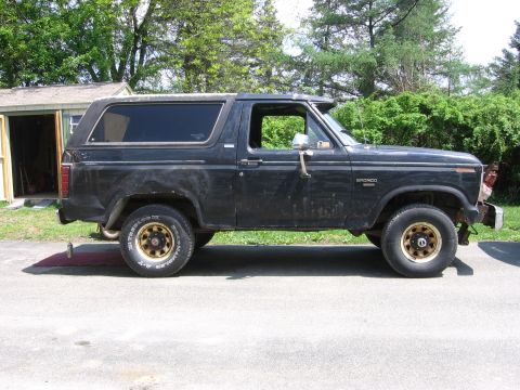 1995 Ford Bronco - This black Ford Bronco is shown from the side, parked in front of a garage and trees.