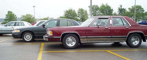 2001 Ford Crown Victoria - A red sedan with tan trim is parked in a lot next to other vehicles.