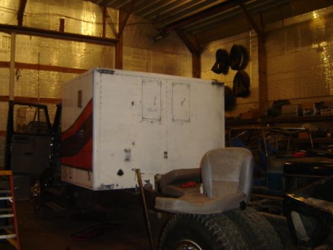 1992 Ford Bronco - A truck cab with a box body and a seat is parked inside a garage, with another vehicle partially visible in the background.