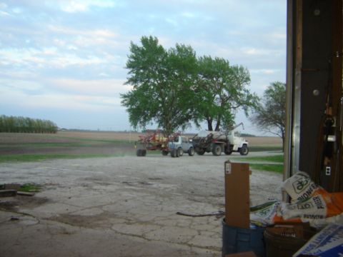 1992 Ford Bronco - Farm vehicles and equipment are parked in a yard with fields and trees in the background under a cloudy sky.