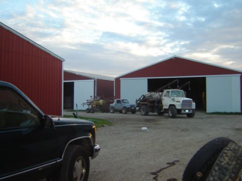 1992 Ford Bronco - A rural farm scene features a white truck, a small SUV, and agricultural equipment situated near large red barns under a cloudy sky.