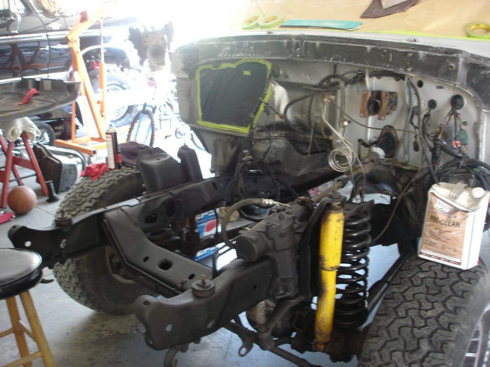 vehicle chassis and engine bay with suspension and wiring exposed, undergoing repair