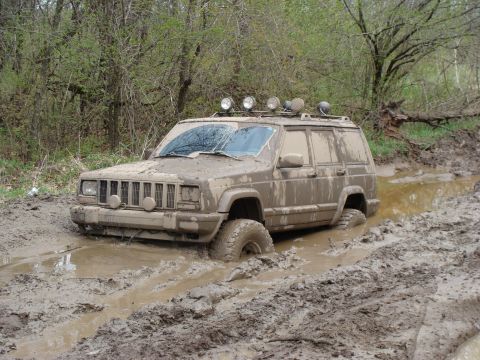 1992 Ford Bronco - This mud-covered Jeep Cherokee is stuck deep in a muddy trail, with only its roof lights visible above the mire.