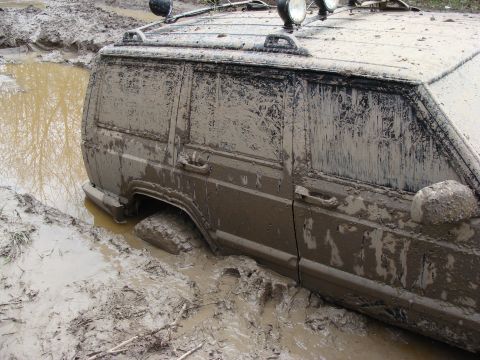 1992 Ford Bronco - Off-road vehicle deeply stuck in thick mud after an apparent recovery attempt.