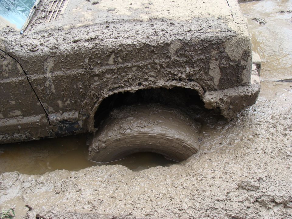 SUV stuck deep in mud, only the top of the wheel and side panel are visible