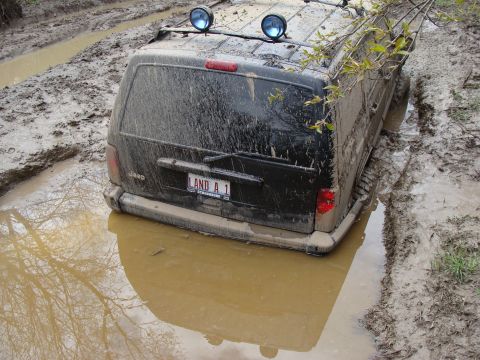 1992 Ford Bronco - A black SUV is deeply stuck in mud, with its rear end submerged in murky water.