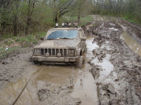 1992 Ford Bronco - This Jeep Cherokee is deeply stuck in a treacherous muddy trail, its tires submerged and body caked in mud.