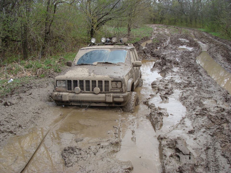 Mud-covered Jeep Cherokee stuck in a muddy trail with roof-mounted lights