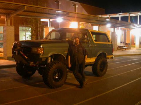 1990 Ford Bronco - Lifted green Ford Bronco with a white top parked at night in an empty lot under building lights, shot from the driver's side. It sits on ta…