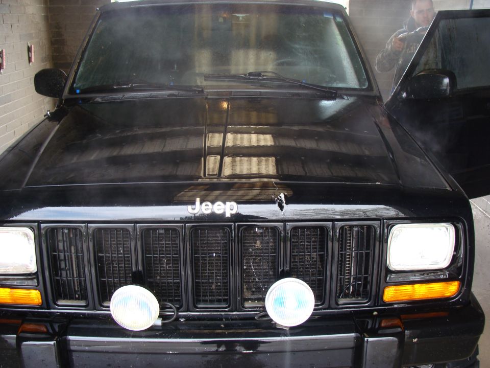 Black Jeep Cherokee XJ front grille with two round fog lights and a person in the open driver's door