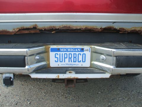 1990 Ford Bronco - Michigan license plate SUPRBC0 is mounted on a rusty rear bumper.