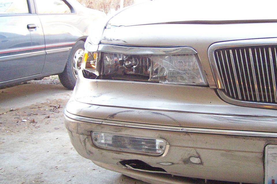 Front corner of tan sedan with damaged bumper and cracked headlight