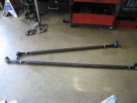 1979 Ford Bronco - Two tie rods, likely for a vehicle's steering system, are laid out on a concrete floor.