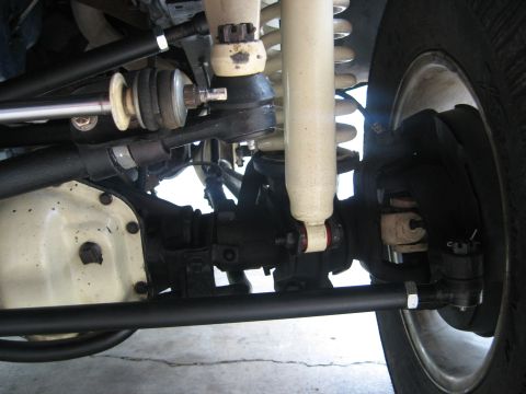 1979 Ford Bronco - Close-up view of the front suspension and steering linkage, including a white shock absorber and differential cover.