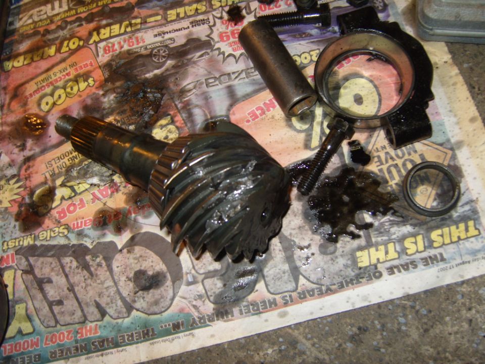 Damaged differential ring gear and pinion shaft with bolts and bearing races on newspaper