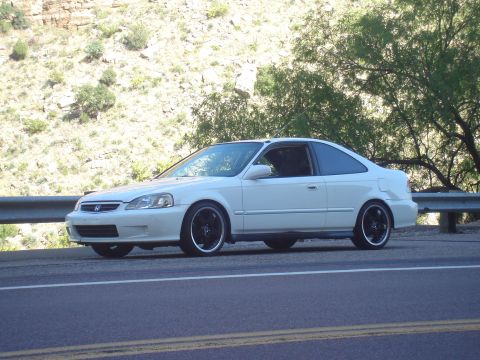 1997 Ford Probe - A white coupe is parked on the side of a road with a guardrail and a rocky hillside behind it.