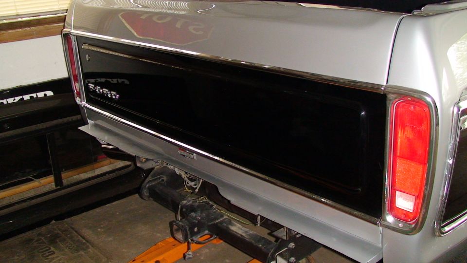 1979 Ford Bronco tailgate with black insert and chrome trim, visible taillight and trailer hitch
