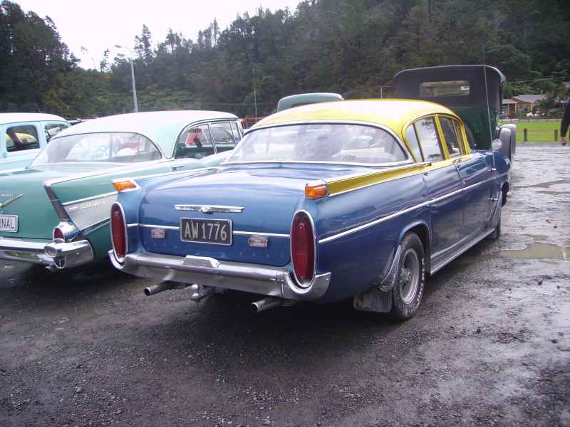 Rear view of a blue sedan with a yellow roof parked next to a teal car. License plate reads AW 1776