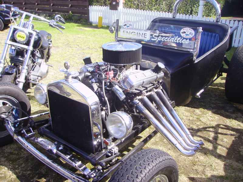 Black T-bucket hot rod with chrome zoomie headers, exposed V8 and blue tuck interior