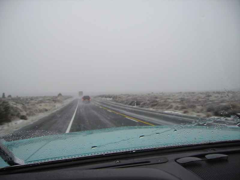 View from inside a car driving on a wet highway with fog and a car ahead