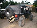 1986 Ford Bronco - This black Jeep Wrangler features a soft top, external roll cage, and a spare tire mounted on the rear. Another vehicle is partially visibl…