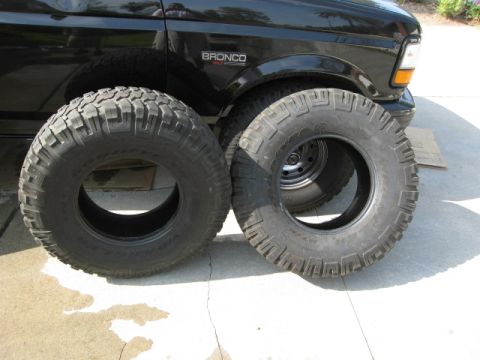 1986 Ford Bronco - Two off-road tires are placed in front of a black Ford Bronco.