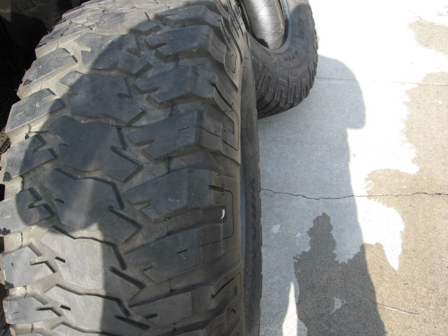 Close-up of a large, knobby off-road tire with a shadow cast on the concrete ground